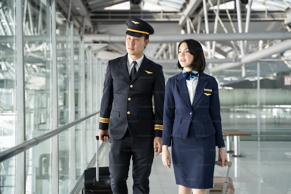 Commercial cabin crew or hostress and pilot occupation concepts. Asian airliner pilot and air hostess walking and talking together in airport terminal to the airplane with smile face and happiness.