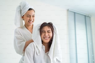 Asian beautiful lesbian couple spending morning leisure time together. Attractive romantic girl in pajamas drying girlfriend's hair after shower on bed in bedroom in house. Homosexual-LGBTQ concept.