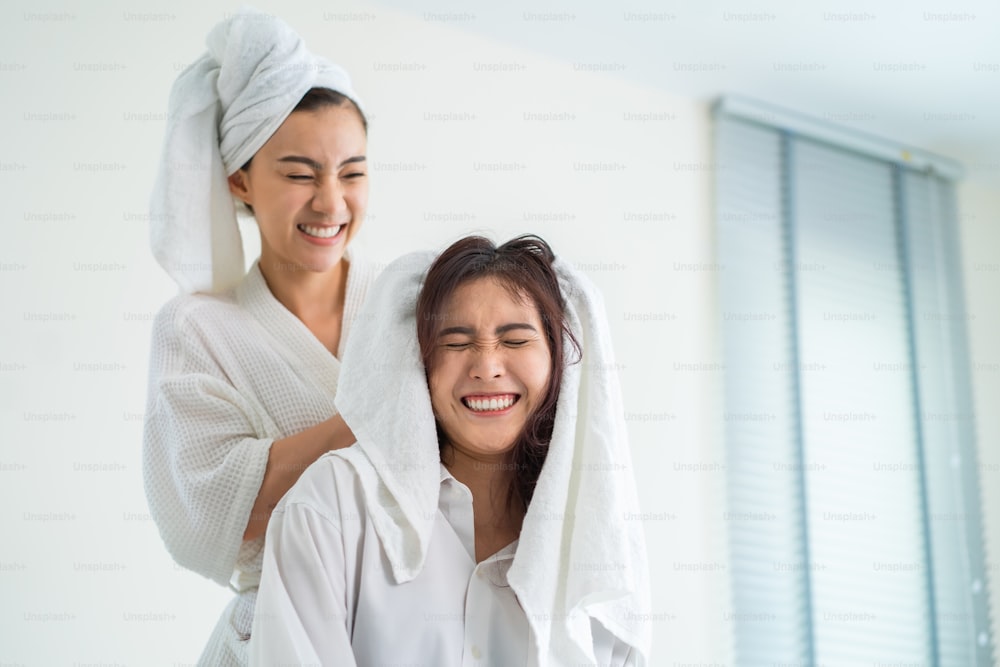 Asian beautiful lesbian couple spending morning leisure time together. Attractive romantic girl in pajamas drying girlfriend's hair after shower on bed in bedroom in house. Homosexual-LGBTQ concept.