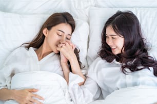 Asian beautiful lesbian couple lying down on bed and hug each other. Attractive romantic lgbt woman gay in pajamas sleeping in early morning time together in bedroom at home. Homosexual-LGBTQ concept.