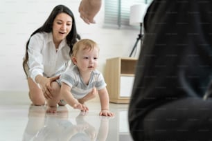 Caucasian baby boy child crawling with parents support in house. Happy family, mother and father help young toddler son learn how to walk and take step on floor to develop skill in living room at home