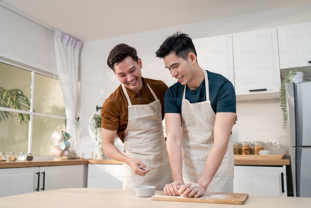 Asian young LGBTQ male gay family enjoy bake bakery in kitchen at home. Attractive handsome romantic man couple wear apron feeling happy and cheerful to spending time cooking foods together in house.