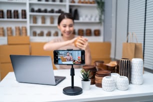 Asiatische schöne Frau verkaufen Vase Produkt online Live-Streaming zu Hause. Junge attraktive Mädchen benutzen Laptop-Computer zeigt Waren zum Kunden und präsentieren Details. Remote Buying und Purchase Shopping-Konzept