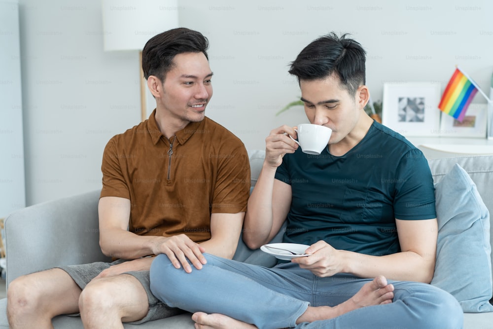 Asian handsome male gay couple drink coffee in early morning together. Attractive romantic lgbt family spending leisure time having breakfast together in living room at home. Homosexual-LGBTQ concept