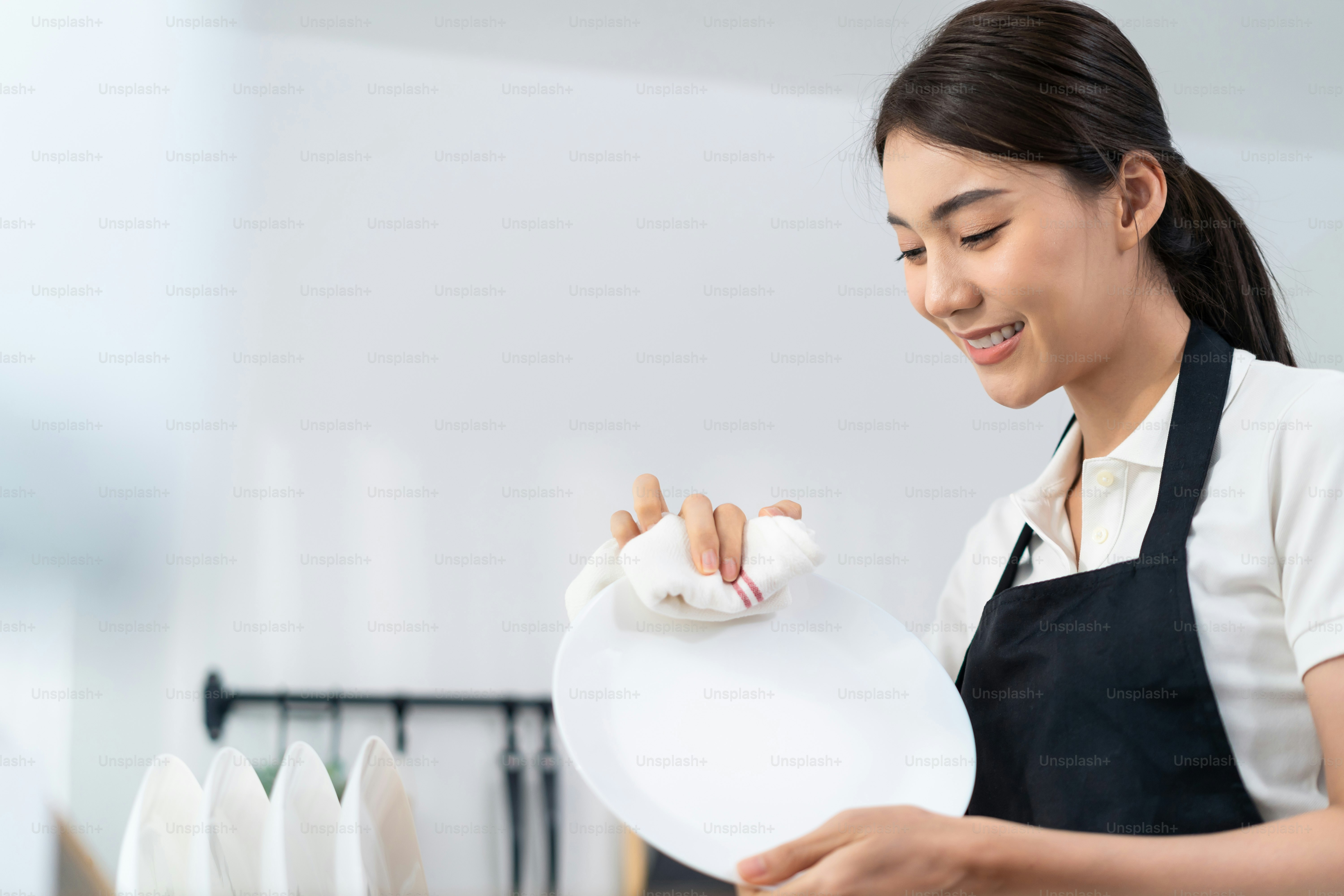 Servizio di pulizia attivo asiatico donna che pulisce in cucina a casa. La bella ragazza delle pulizie si sente felice e pulisce i piatti dopo il lavaggio per le faccende domestiche o le faccende domestiche.