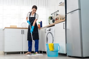 Asian active cleaning service woman worker cleaning in kitchen at home. Beautiful young girl housekeeper cleaner feel happy and mopping on floor working for housekeeping housework or chores in house.