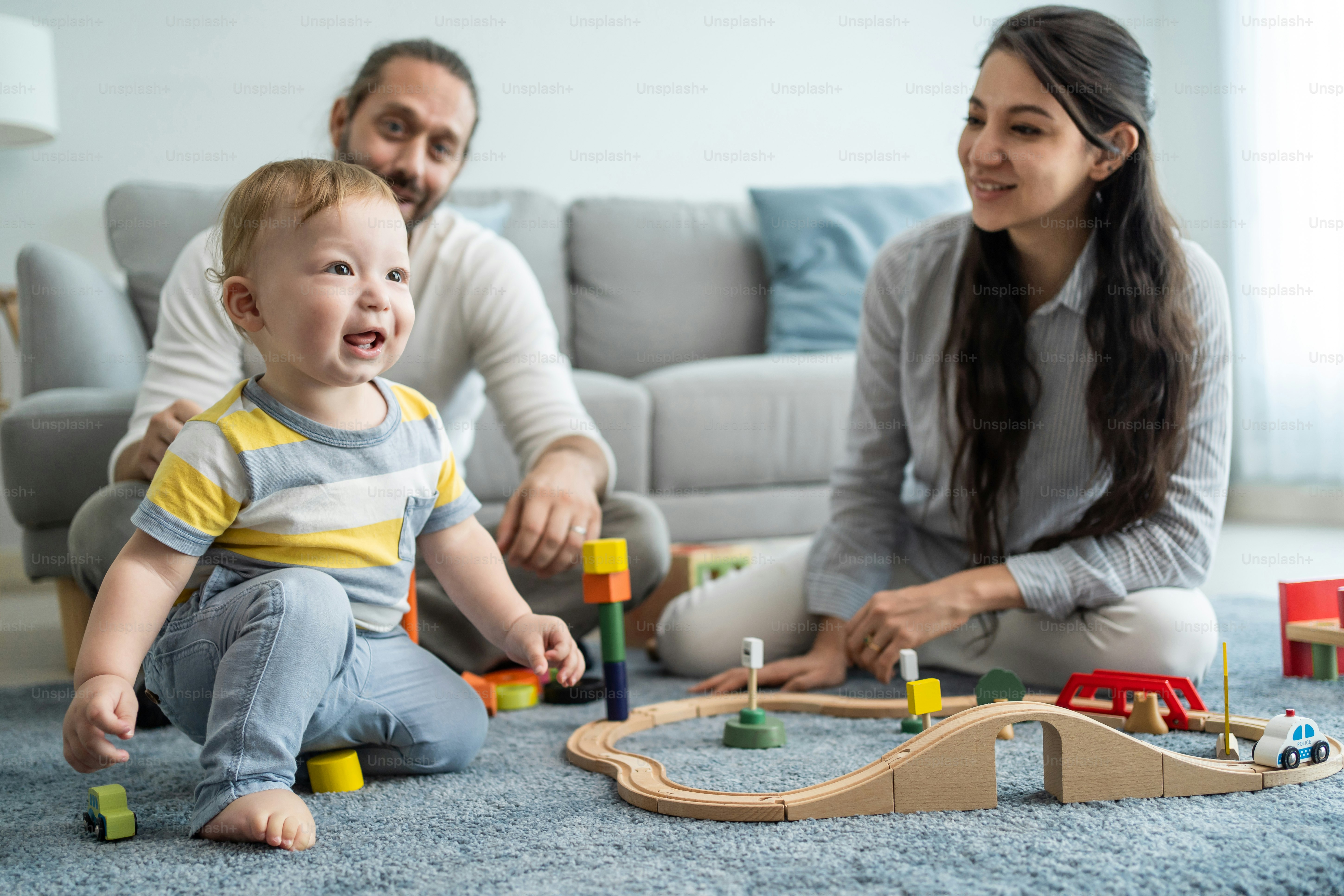 Caucasian happy loving parent play with baby toddler in living room. Attractive couple mother and father spend time with young little infant son child in house. Activity relationship at home concept.