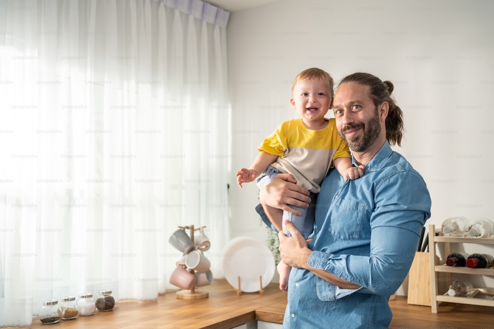 Portrait of Caucasian loving father hold baby boy child in living room. Happy family, attractive caring young dadd carry his toddler son on hands with happiness in house. Activity relationship at home