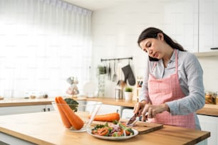 Caucasian woman talk on phone while cooking salad in kitchen at home. Young beautiful girl enjoy communicate online on smartphone and eating vegetables healthy foods to diet for health care in house.