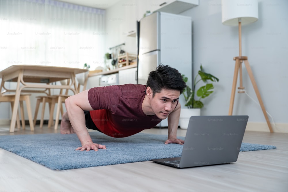 Asian handsome active young man doing push up on floor in living room. Attractive male in sport cloth spend leisure activity time to exercise and workout on holiday at home. Healthy lifestyle concept.