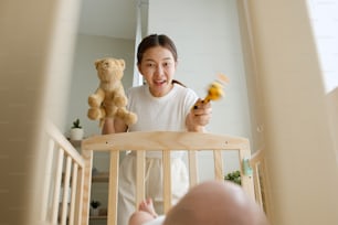 Young Asian mother playing doll with her newborn baby on crib joyfully
