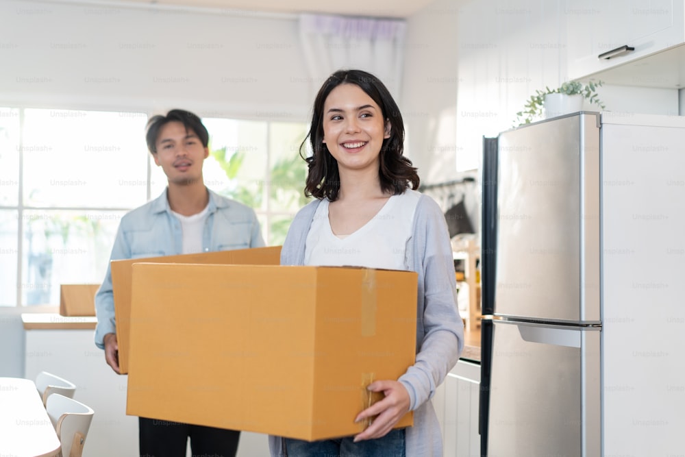 Portrit of Asian young happy new marriage couple moving to new house. Attractive romantic man and woman holding box parcel and suitcase with happiness and love. Family-Moving house relocation concept.