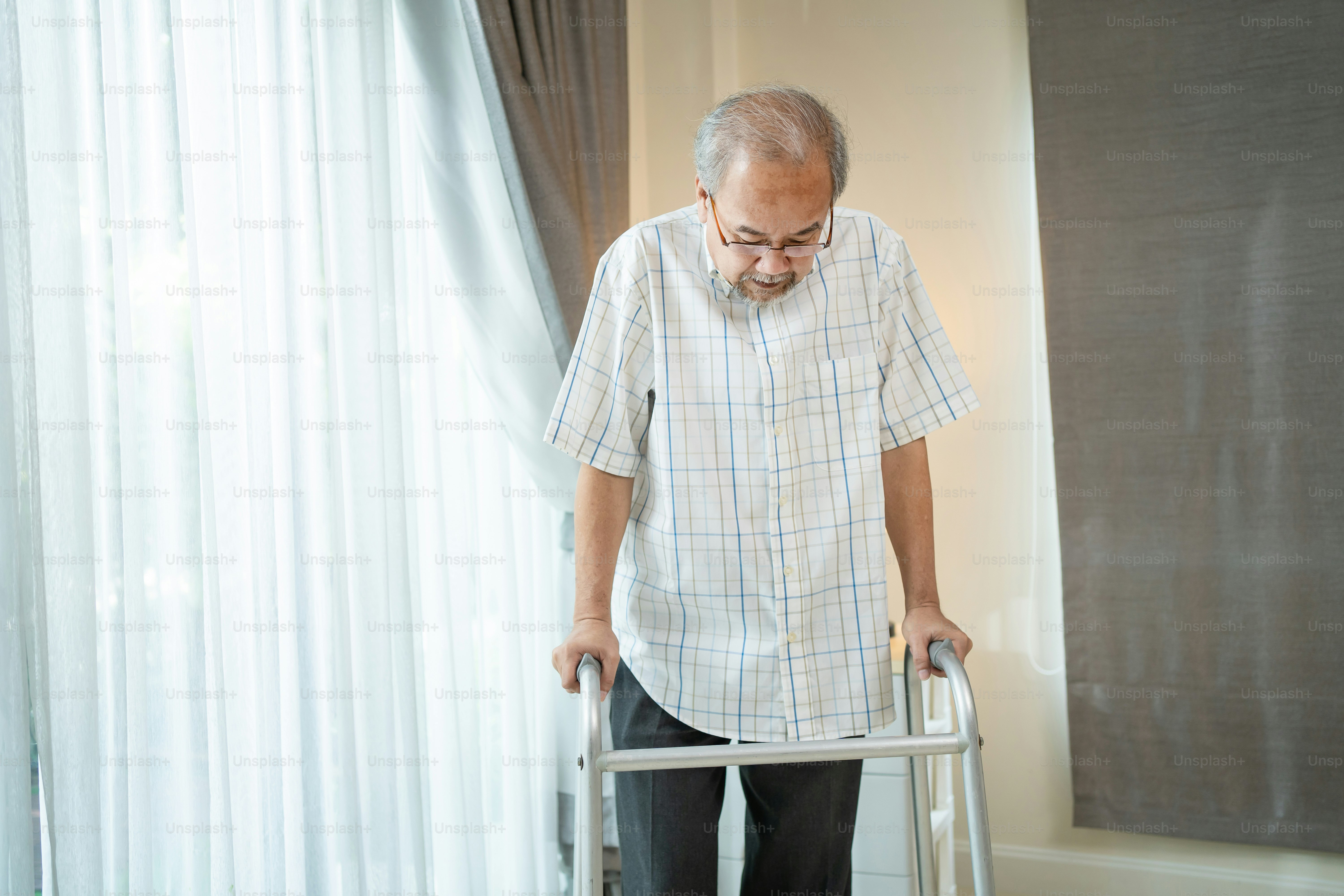 Asian Senior elderly man patient walking slowly with walker in house. Mature  older grandfather doing physical therapy alone with cane in living room at  home. Medical Health care insurance concept. photo –