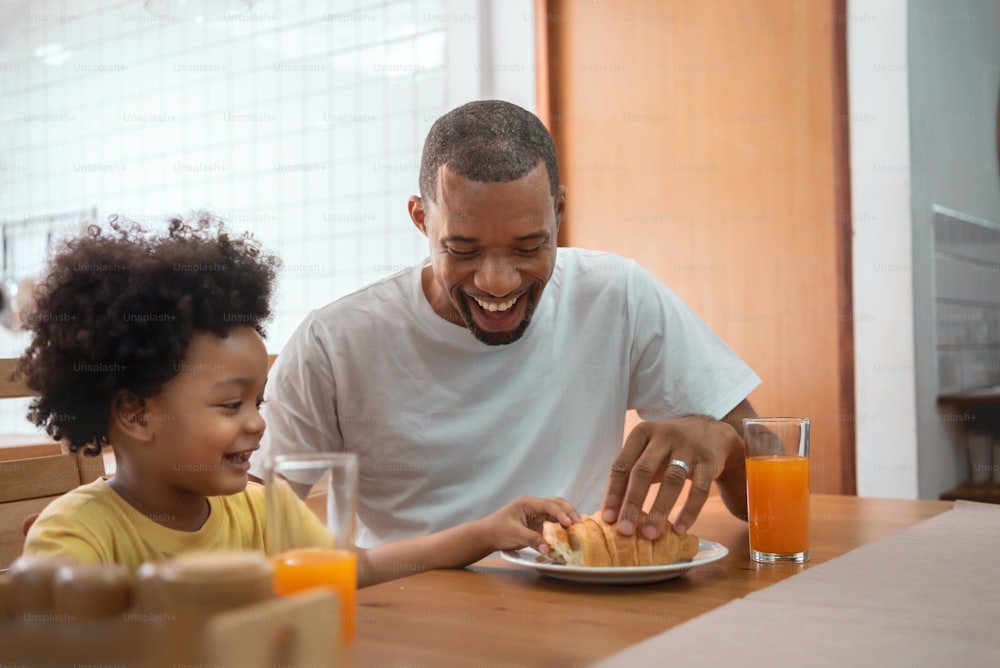 Happy African American Father and little son playing together in breakfast at dining table