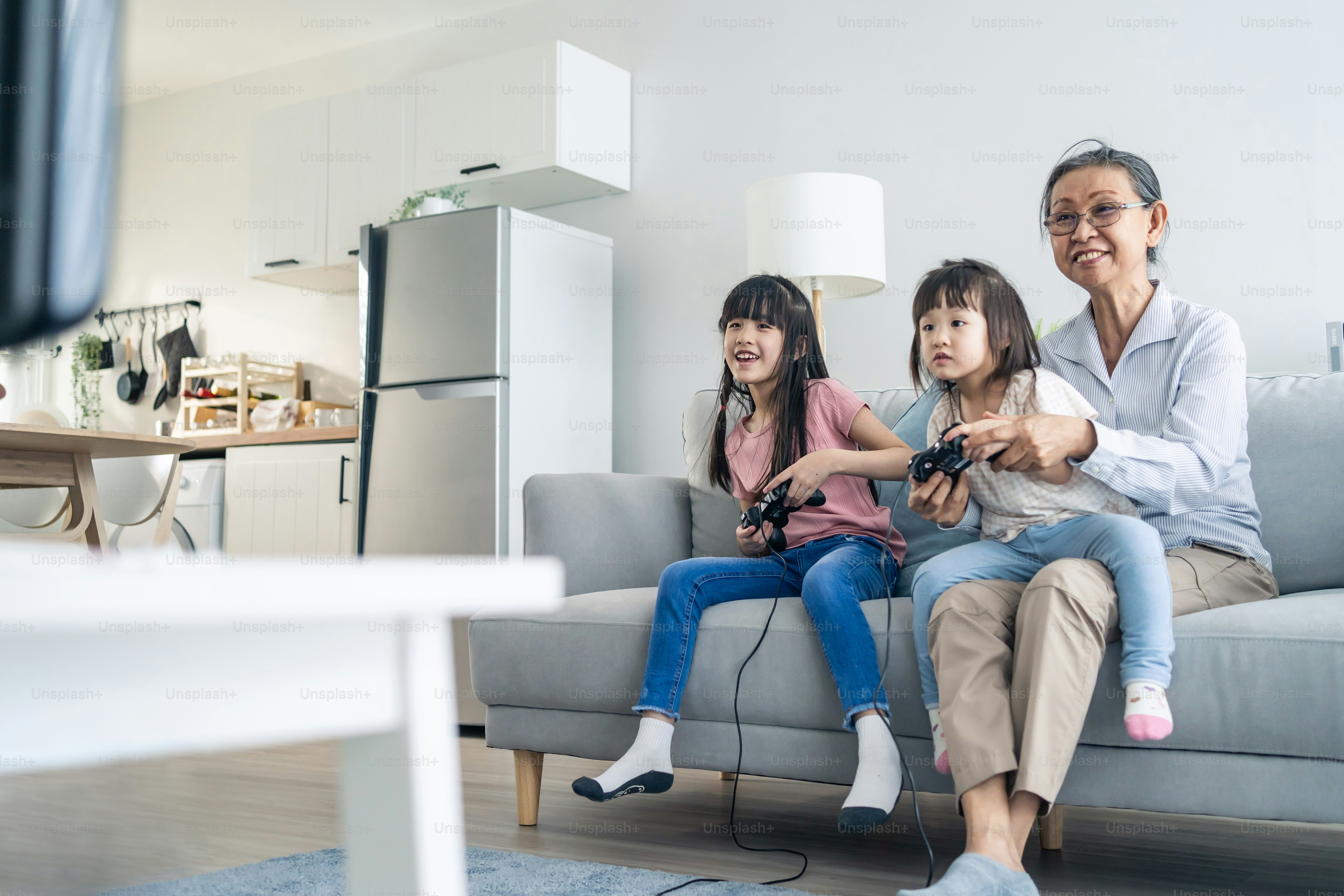 La familia feliz asiática se queda en casa, la abuela juega con la niña. Mujer mayor amorosa mayor mayor juega videojuegos frente al televisor con la nieta de los niños pequeños en la sala de estar juntos.