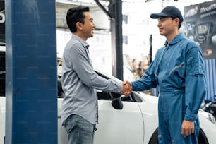 Asiatischer Kfz-Mechaniker Handschlag mit Kunde in der Garage. Kfz-Service-Manager, der in der Mechanikerwerkstatt arbeitet, fühlt sich glücklich und Erfolg nach Überprüfung und Wartung Automotor für den Kunden.