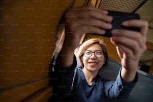 Happy Asian woman tourist wear glasses taking a selfie with smartphone Inside a train. Smiling face. Travel Concept.
