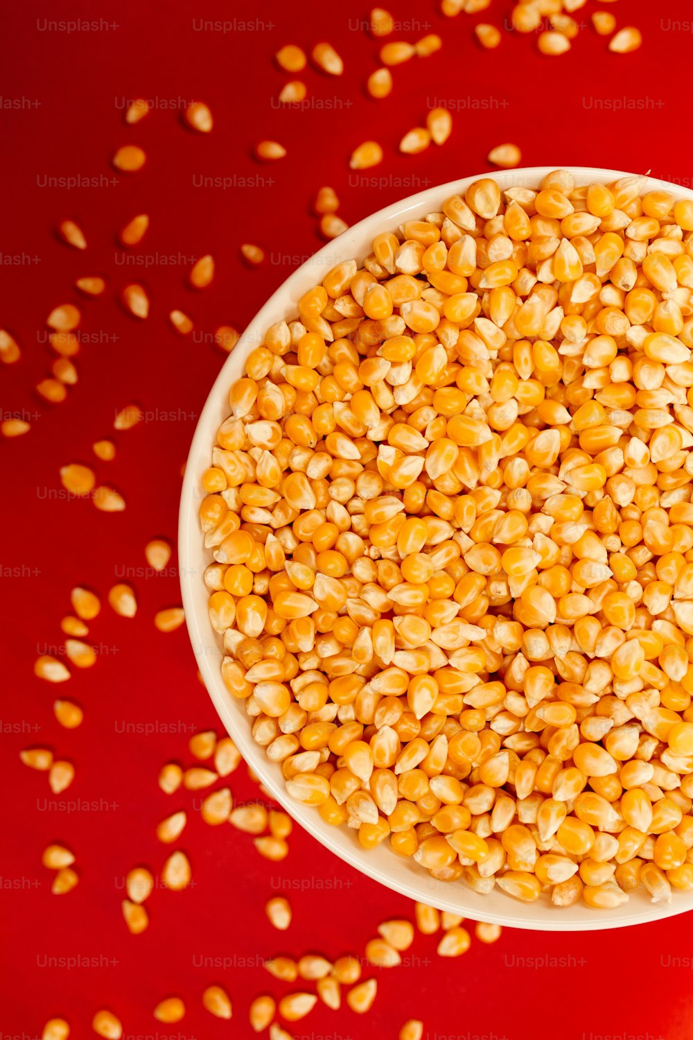 Un tazón blanco lleno de granos de maíz sobre una superficie roja