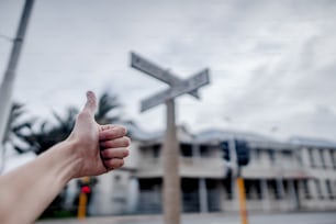 Una persona dando un pulgar hacia arriba con un letrero de la calle en el fondo