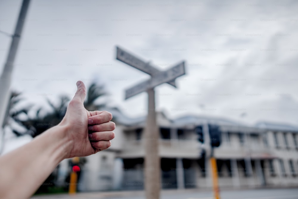 uma pessoa dando um polegar para cima com uma placa de rua ao fundo