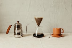 uma mesa coberta com uma cafeteira ao lado de uma xícara de café