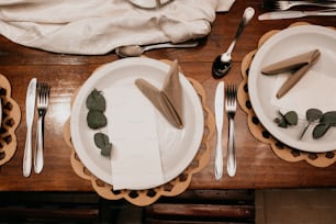 a wooden table topped with white plates and silverware