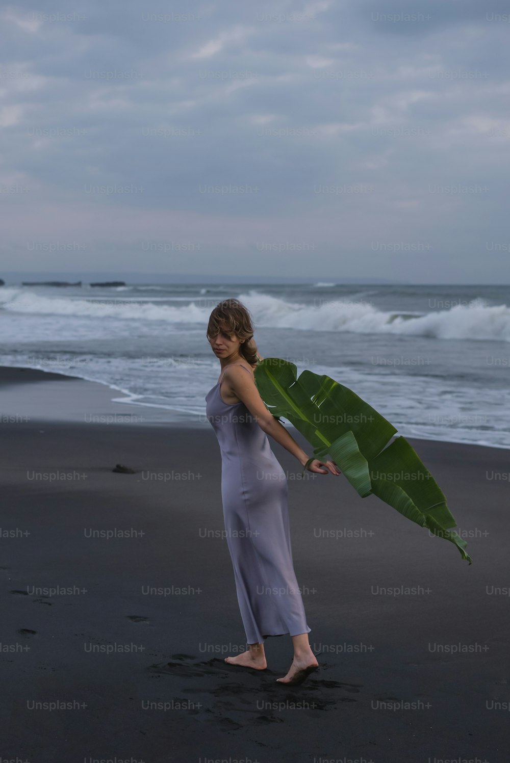 a woman holding a large banana leaf on a beach