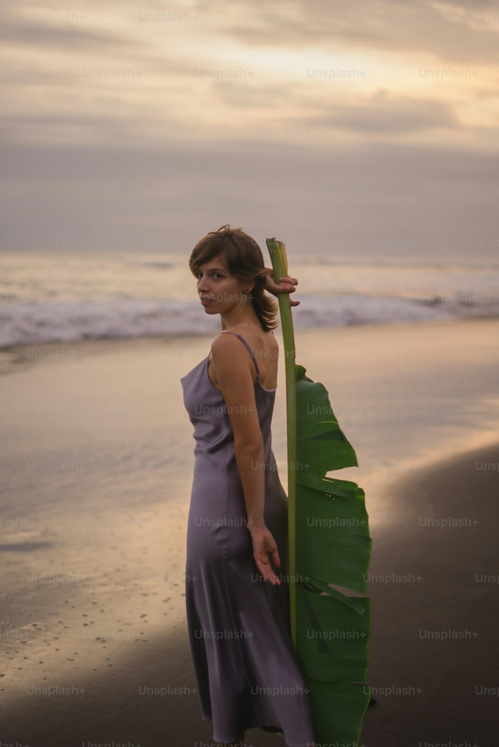 a woman standing on a beach holding a banana leaf