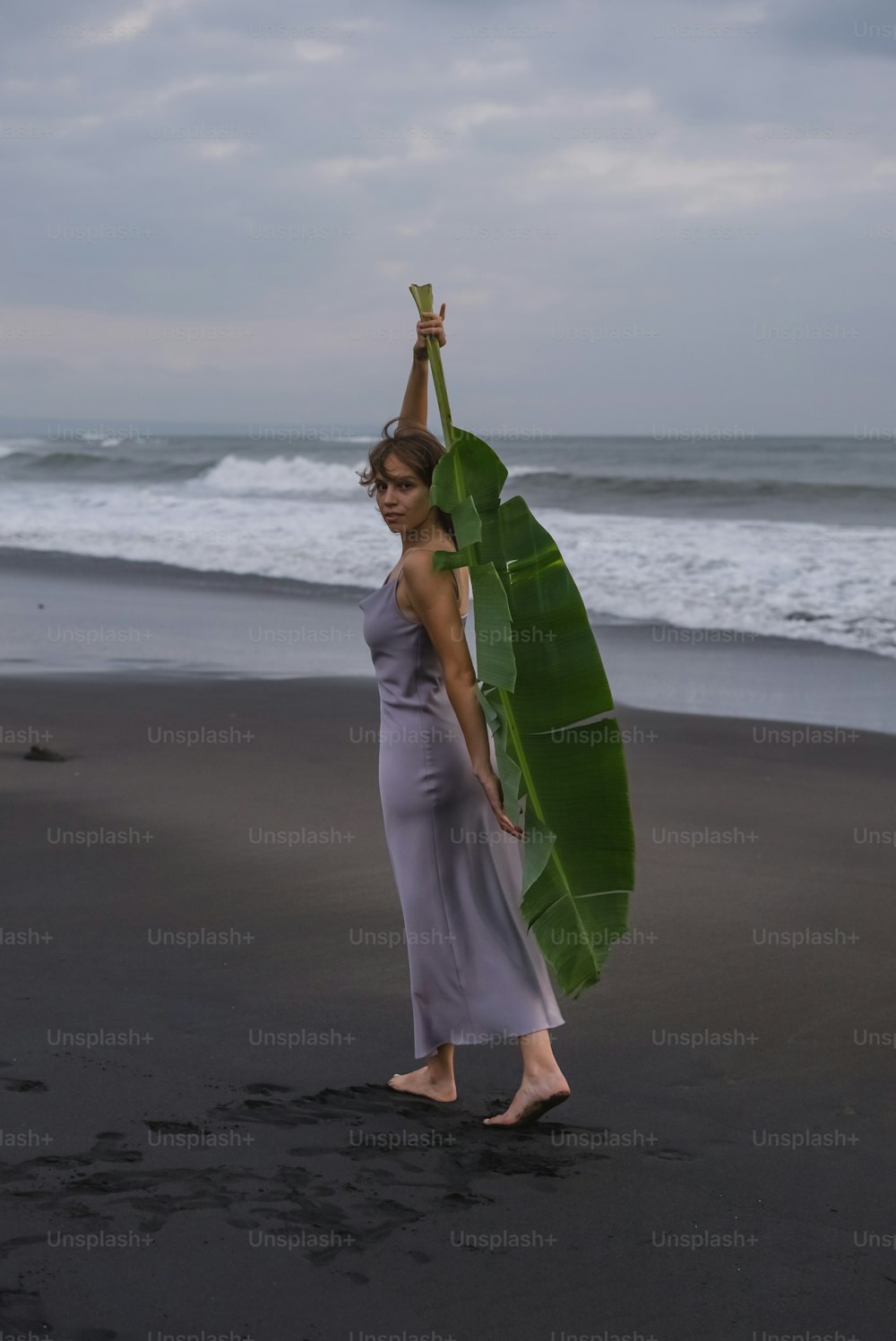 a woman holding a large banana leaf on a beach