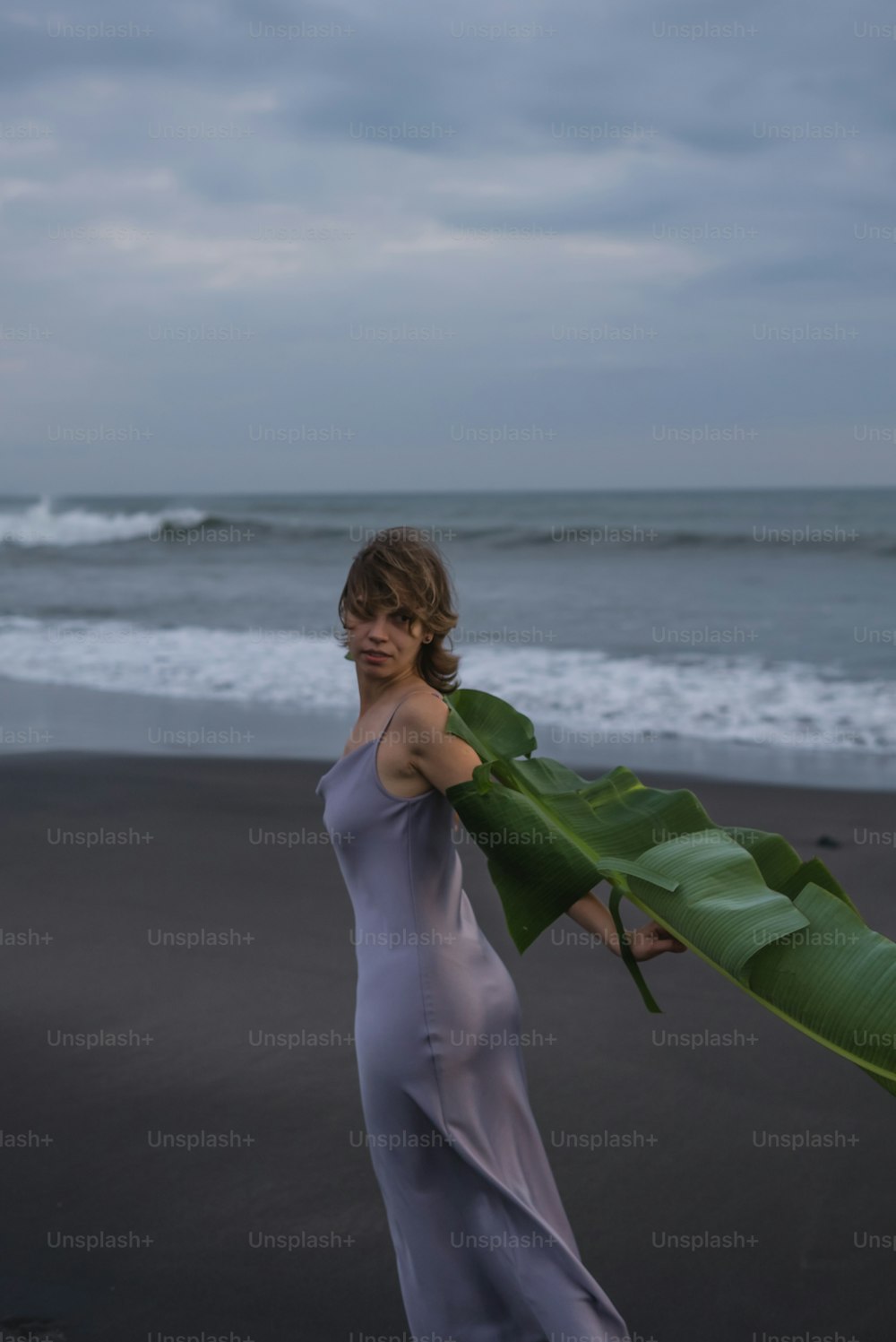 a woman holding a large green leaf on a beach