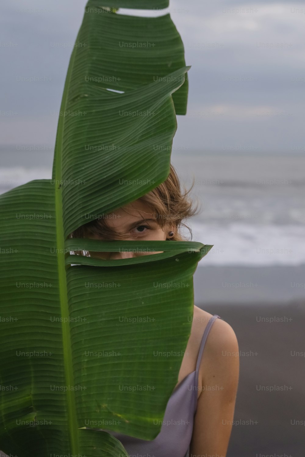 a woman hiding behind a large green leaf