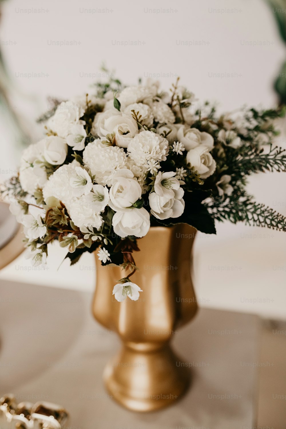 Un jarrón de oro lleno de flores blancas encima de una mesa