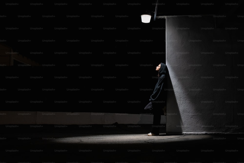 Un hombre apoyado contra una pared en la oscuridad