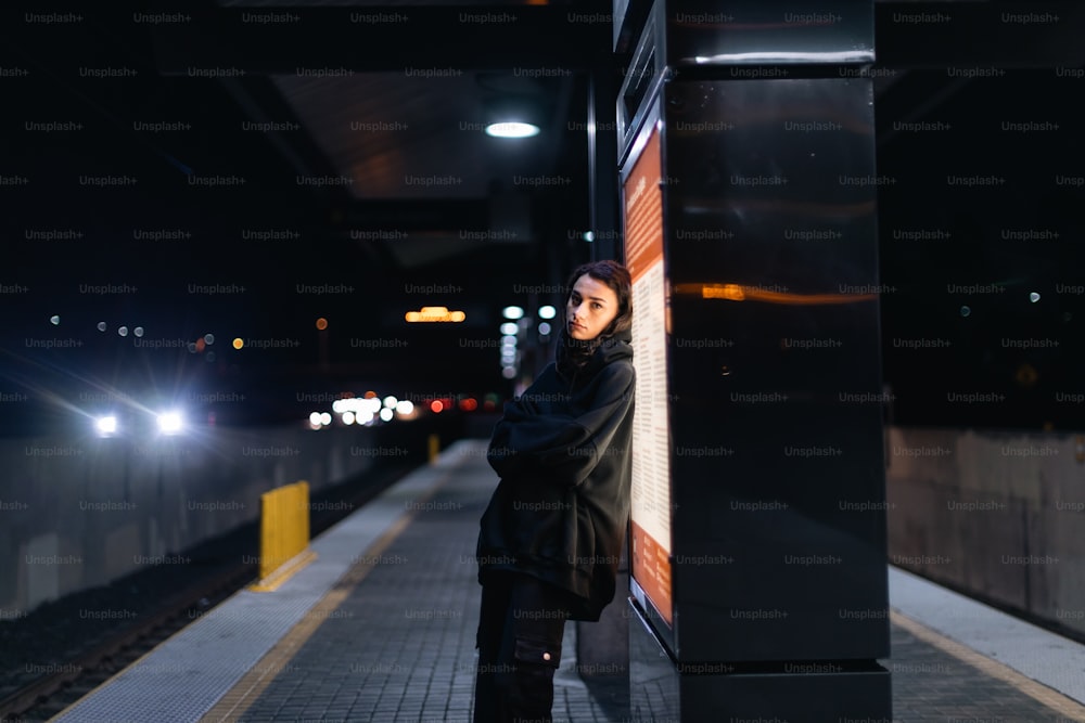 a woman leaning against a wall at a train station