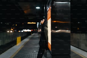 a woman leaning against a wall on a train platform