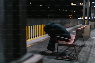 una persona seduta su una panchina con la testa bassa