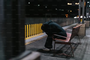 une personne assise sur un banc, la tête baissée