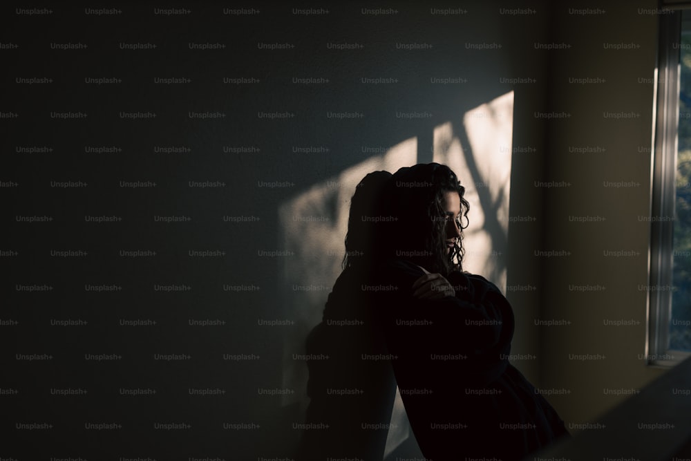 uma mulher em pé em um quarto escuro ao lado de uma janela
