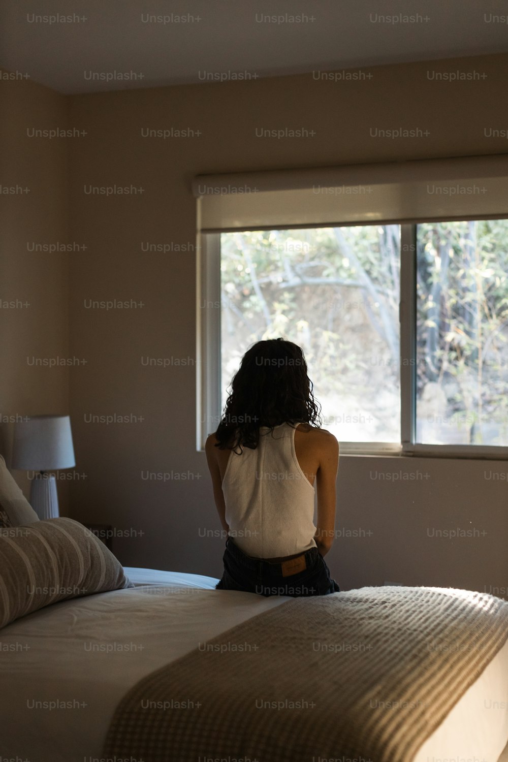 Una mujer sentada en una cama mirando por una ventana