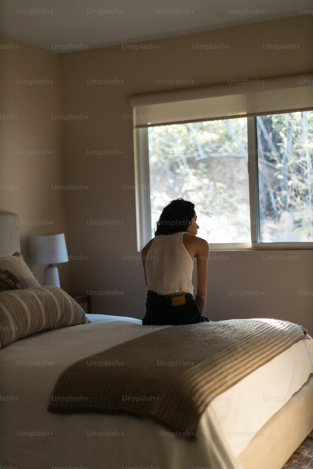 Una mujer sentada en una cama mirando por una ventana