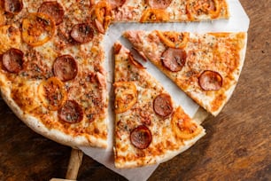 eine Peperoni-Pizza, die auf einem Holztisch in Scheiben geschnitten wird