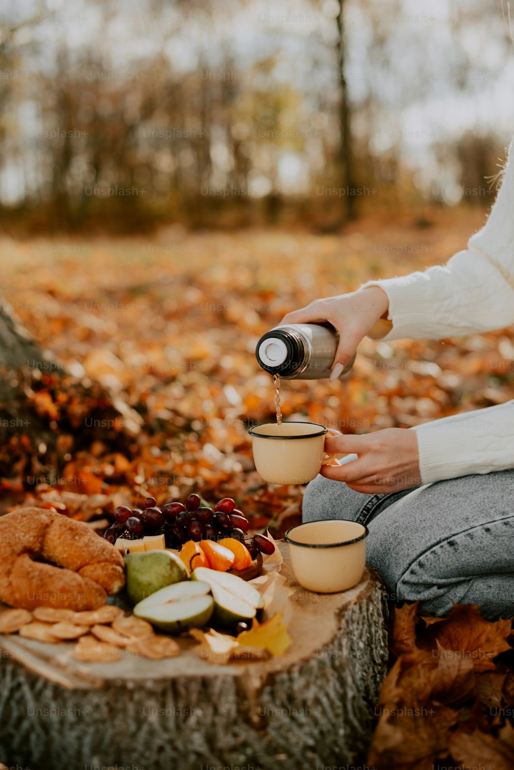 a woman sitting on a tree stump pouring a cup of coffee