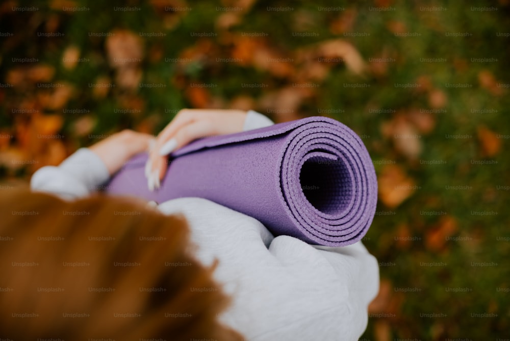 uma mulher segurando um tapete de yoga roxo em suas mãos