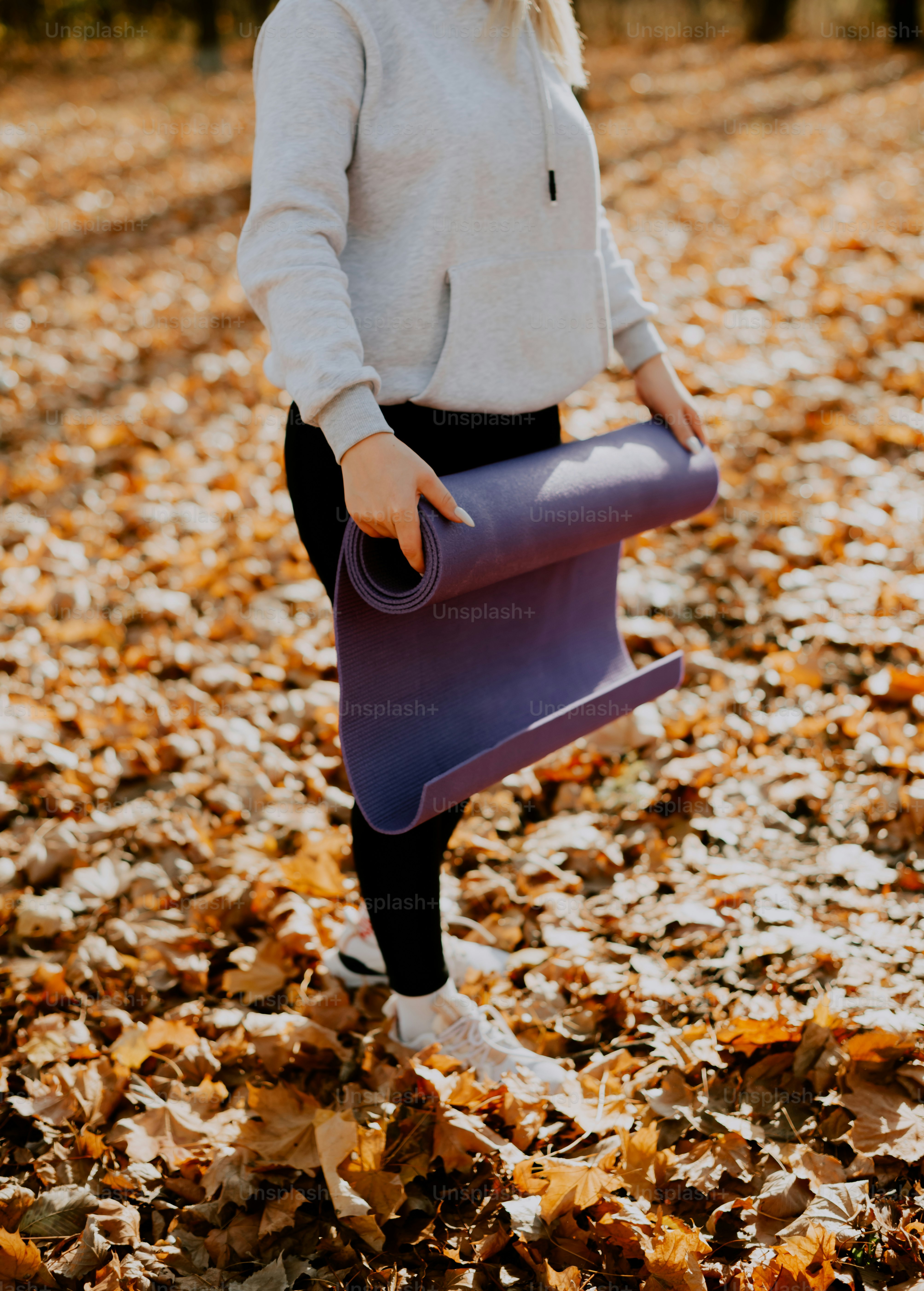 a woman holding a purple yoga mat in the leaves