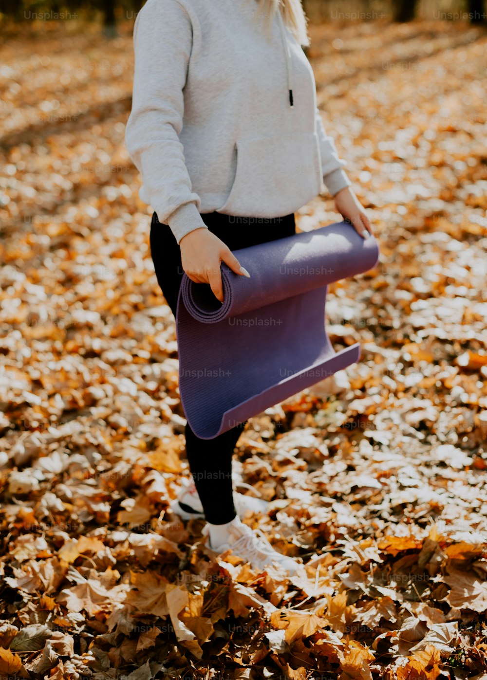 a woman holding a purple yoga mat in the leaves