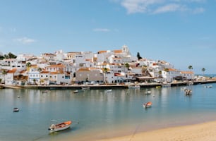 a beach with boats in the water and houses on a hill in the background