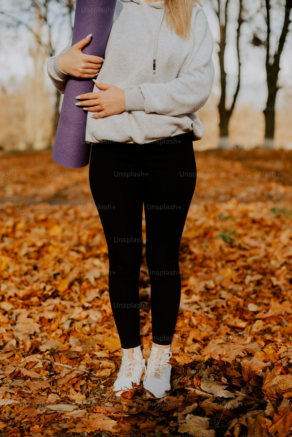 uma mulher em pé em folhas segurando um tapete de ioga