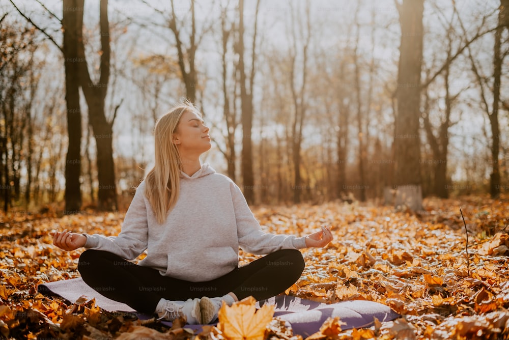 a woman in a white sweater and black pants meditates on a blanket in