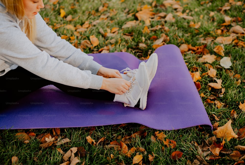 a woman is sitting on a purple mat on the grass