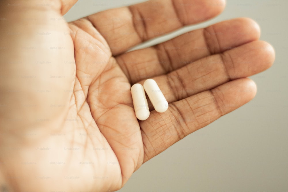 a person holding two pills in their hand